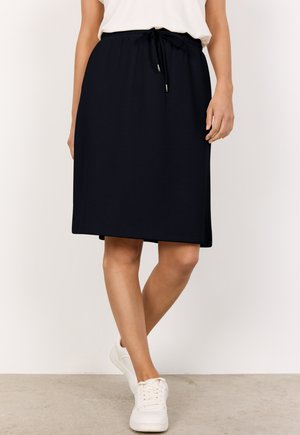 Marineblauer knielanger Rock aus weichem Stoff, mit elastischem Bund und Kordelzug sowie einem geraden Schnitt. Kombiniert mit weißen Sneakern.