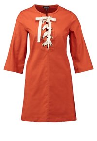 Robe en coton orange avec un col rond, des manches trois-quarts, un devant à lacets avec des rubans crème, et des accents en œillets métalliques.