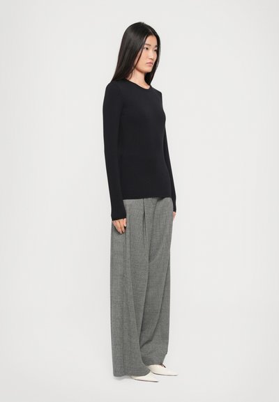 Black long-sleeve top, fitted design; paired with gray wide-leg trousers featuring a check pattern. Model wears pointed white shoes.