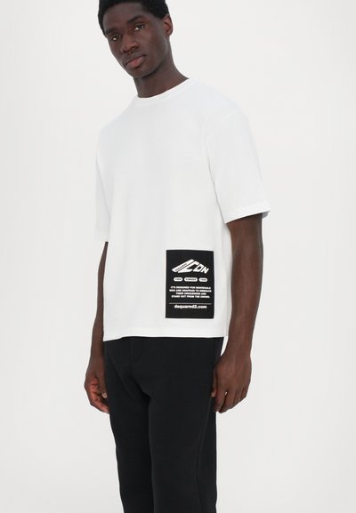Hvid bomulds T-shirt med afslappet pasform, kortærmede og et sort label på venstre side med hvid tekst og grafik.