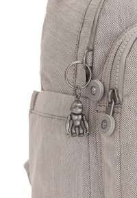 Lys grå rygsæk med diagonal tekstur, der har et metalvedhæng, sølvhardware og lynlåse med runde trækstænger.