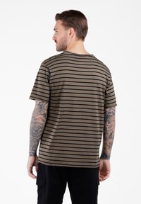 Camiseta de manga corta a rayas en verde oliva con rayas negras, con cuello redondo; la tela parece suave y ligera.