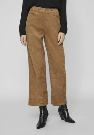 Pantalones de pana marrón de pierna ancha, con cintura alta y cierre de botón, combinados con botas negras de tobillo. Textura suave con un sutil brillo.