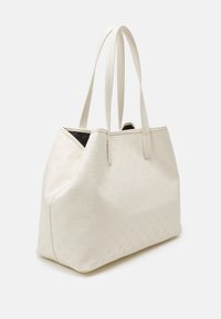 Stor cremefarvet totebag lavet af tekstureret materiale, med præget logo mønstre, to lange håndtag og en struktureret form.