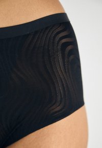 Černé kalhotky s hladkým, strukturovaným designem s vlnitými vzory. Dokončeny pevným černým elastickým pasem.