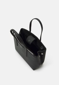 Sac fourre-tout en cuir noir avec deux poignées, ouverture supérieure, poche intérieure zippée et fermeture à bouton-pression. Texture lisse et design minimaliste.