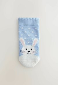 Chaussette bleu clair présentant un visage de lapin blanc avec des moustaches noires et des accents roses. Il y a des pois blancs au-dessus du motif du lapin.