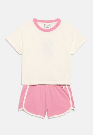 Camiseta blanca de manga corta y corte corto con cuello rosa y pantalones cortos deportivos rosas con ribete blanco, colocados sobre un fondo blanco.