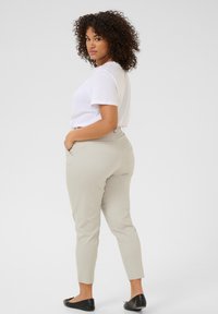 Pantaloni attillati beige chiaro abbinati a una camicia bianca a maniche corte. Il tessuto appare liscio, con una vestibilità slim e tasche laterali.
