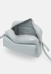 Borsa a tracolla in pelle azzurro chiaro con texture intrecciata, chiusura con zip, tasche interne e finitura liscia. Include una tracolla regolabile.