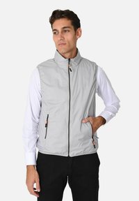 Gilet grigio senza maniche realizzato in tessuto leggero, con colletto alto, zip frontale e due tasche con zip dotate di dettagli arancioni.