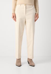 Helle beige, gerippte Hose mit geradem Schnitt, ausgestattet mit einem Knopfverschluss vorne und seitlichen Taschen, kombiniert mit taupefarbenen Ankle Boots.