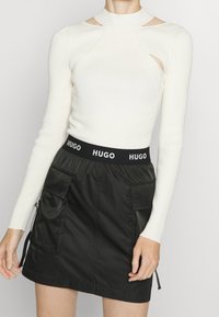 Top bianco a maniche lunghe a coste con dettagli ritagliati, abbinato a una gonna nera con fascia elastica HUGO in vita e tasche laterali.
