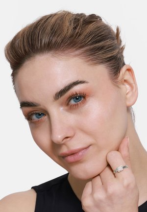 Silberner Ring mit einem quadratischen Edelstein, der ein gewundenes Banddesign aufweist, am Finger getragen. Das Subjekt hat glatte Haut, leichtes Make-up und braunes Haar.
