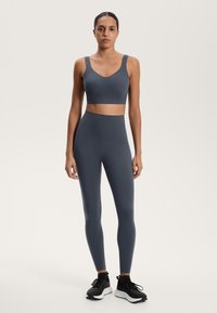 Mörkgrå sportbh och högmidjade leggings gjorda av elastiskt material. Modellen bär svarta träningsskor. Slät textur och figurnära design.