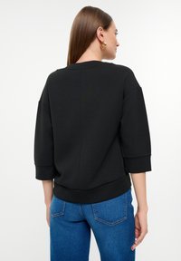 Schwarzes Sweatshirt mit Rundhalsausschnitt, Dreiviertelärmeln und geripptem Saum. Der Stoff wirkt weich und hat eine glatte Textur.