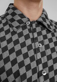 Camisa a cuadros gris y negra con cuello abotonado, presenta botones de metal, una mezcla de algodón y un acabado texturizado.