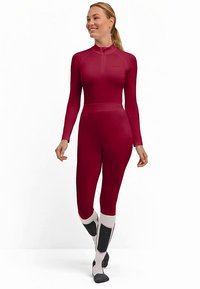 Czerwony kombinezon do nurkowania z długim rękawem, dopasowanym krojem, wysokim kołnierzem i suwakiem do ćwiartki. Posiada kontrastujące białe i szare buty z ciemnymi akcentami.
