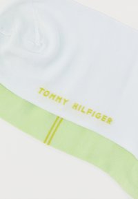 Λευκή αθλητική κάλτσα με ανοιχτό πράσινο περιθώριο, που διαθέτει κίτρινη ρίγα και λογότυπο "TOMMY HILFIGER" κεντημένο με κίτρινο στη πλευρά.