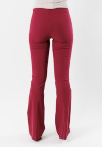 Pantaloni rossi a zampa d'elefante realizzati in tessuto leggero, caratterizzati da una texture liscia e una vita aderente. Il design enfatizza una silhouette fluida.