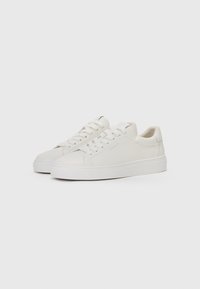 Adidași din piele albă cu o textură netedă, vârf rotund și sistem de prindere cu șireturi. Prezintă o marcaj minimal pe laterale și o talpă groasă albă.
