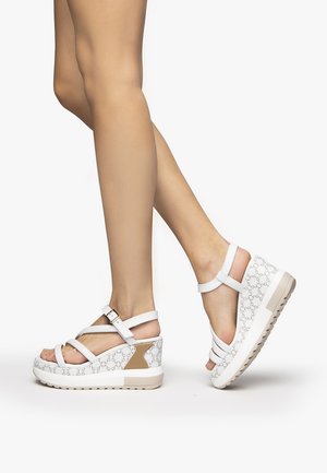 White wedge sandals with multiple straps and a patterned upper. The design features a tan accent on the heel and a textured sole.