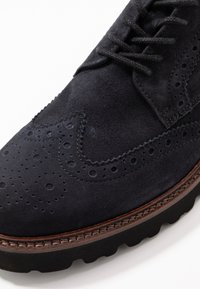 Dunkle marineblaue Wildleder Derby Schuhe mit durchbrochenem Wingtip-Design, strukturiertem Obermaterial und einer kontrastierenden braunen Sohle mit strukturiertem Rand.