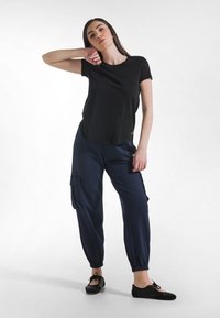 Camiseta negra de manga corta combinada con pantalones cargo azul marino con puños elásticos, bolsillos laterales y bailarinas negras. Diseño liso y casual.