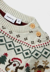 Maglione beige con motivo festivo che presenta renne e alberi. Collo a costine, bottoni naturali e decorazioni a diamante lavorate a maglia.