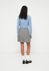 Pulover bleu deschis, fustă plisată gri cu model în carouri houndstooth, pantofi negri și șosete albe. Material neted, croială mulată.