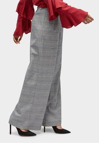 Pantalons larges en vichy gris avec une tissu léger, présentant un motif à carreaux marqué et une coupe ajustée. Associés à des escarpins noirs à bouts pointus.