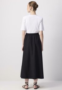 Jupe noire longueur cheville avec une taille élastique, associée à une chemise blanche à manches courtes. Design simple, texture lisse et accents minimalistes.