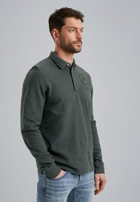 Lange mouwen polo shirt in donkergroene katoenmix. Heeft een kraag, een sluiting met drie knoppen en een geborduurd logo op de borst.