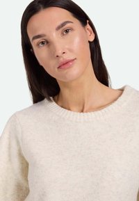 Helles Cremepullover aus weichem, strukturiertem Material. Verfügt über einen gerippten Kragen und eine leicht übergroße Passform mit sichtbaren Nähten.