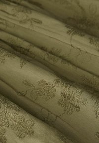 Olivgrüner Stoff mit zarten gestickten Blumenmustern, sanft gefaltet, um die Textur und die feinen Nähdetails zu präsentieren.