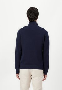 Marineblauwe gebreide trui met een hoge hals, geribbelde manchetten en onderrand. Glad textuur, aansluitend ontwerp en geen zichtbare logo's of patronen.