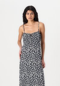 Rochie maxi florală cu fundal bleumarin, având flori albe, bretele ajustabile și un corp strâns cu detaliu tip chei.