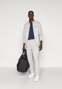 Γκρι ζακέτα με φερμουάρ και παντελόνι φόρμας από φλις υλικό, σε συνδυασμό με μπλε ναυτικό T-shirt. Μαύρη τσάντα duffel και λευκά αθλητικά παπούτσια ολοκληρώνουν την εμφάνιση.