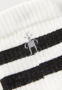 Neulotut sukat, joissa on valkoinen pohja mustilla vaakaraitoilla ja pieni harmaa porokuvio ylhäällä. Kudos näyttää pehmeältä.