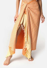 Orange og gul mønstret omslagsskjørt med diamantmotiver, der har en båndlukning og frynset kant, lavet af letvægtsstof.