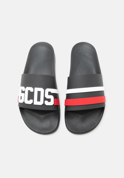Ζευγάρι μαύρων σανδαλιών τύπου σλάιντ με υφασμένα πέλματα, το αριστερό λουράκι έχει λευκό κείμενο "GCDS" και το δεξί λουράκι λευκές και κόκκινες οριζόντιες ρίγες.