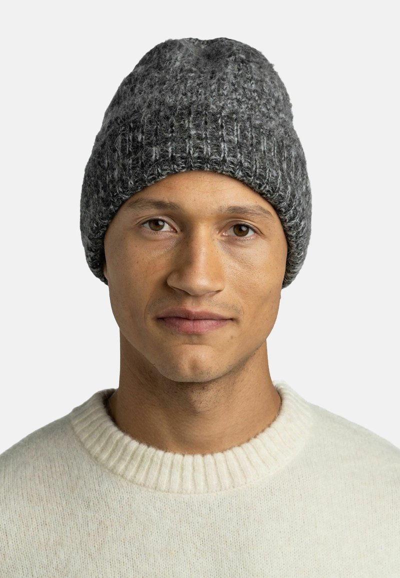 Grey knit beanie with a textured pattern, worn by a person in a light-colored, ribbed sweater against a plain background.