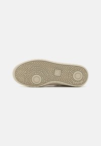 Sole di sneaker beige con un motivo a spina di pesce testurizzato, accenti circolari, logo del marchio e piccole sezioni rialzate per una migliore aderenza.