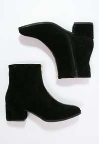Bottes de cheville en suede noir avec un talon épais, fermeture éclair latérale et texture lisse. Comprend un bout pointu et des accents de fermeture éclair dorés.