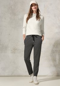 Pull gris clair à côtes, pantalon grisonnant à rayures avec cordon de serrage, et baskets montantes blanches. Design simple avec poches fonctionnelles.