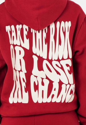 Rode hoodie met witte, golvende tekst "NEEM HET RISICO OF VERLOSL DE KANS" op de achterkant. Zacht fleece materiaal en verstelbare capuchon.