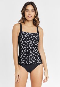 Zwart-witte tankini-top met stippen, vierkante halslijn, gerimpeld voorpand en verstelbare banden, gecombineerd met zwarte bikini-broekjes.