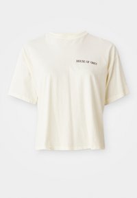 Crème-kleurig T-shirt met korte mouwen, gemaakt van zacht katoen en met een ronde hals. Voorzien van zwarte tekst "HOUSE OF OBEY" op de linkerkant van de borst.