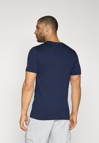 Camiseta ajustada de color azul marino en mezcla de algodón, con mangas cortas, cuello redondo y un pequeño logo en contraste en la manga izquierda.