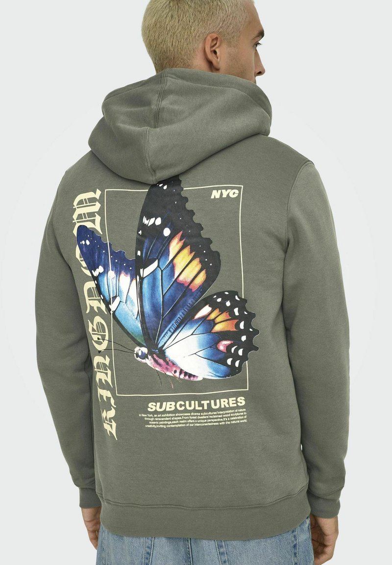 Olijfgroene hoodie met een grote vlinderafbeelding op de achterkant, met kleurrijke vleugels. De tekst bevat "NYC" en "SUBCULTURES." Zachte, gestructureerde stof.